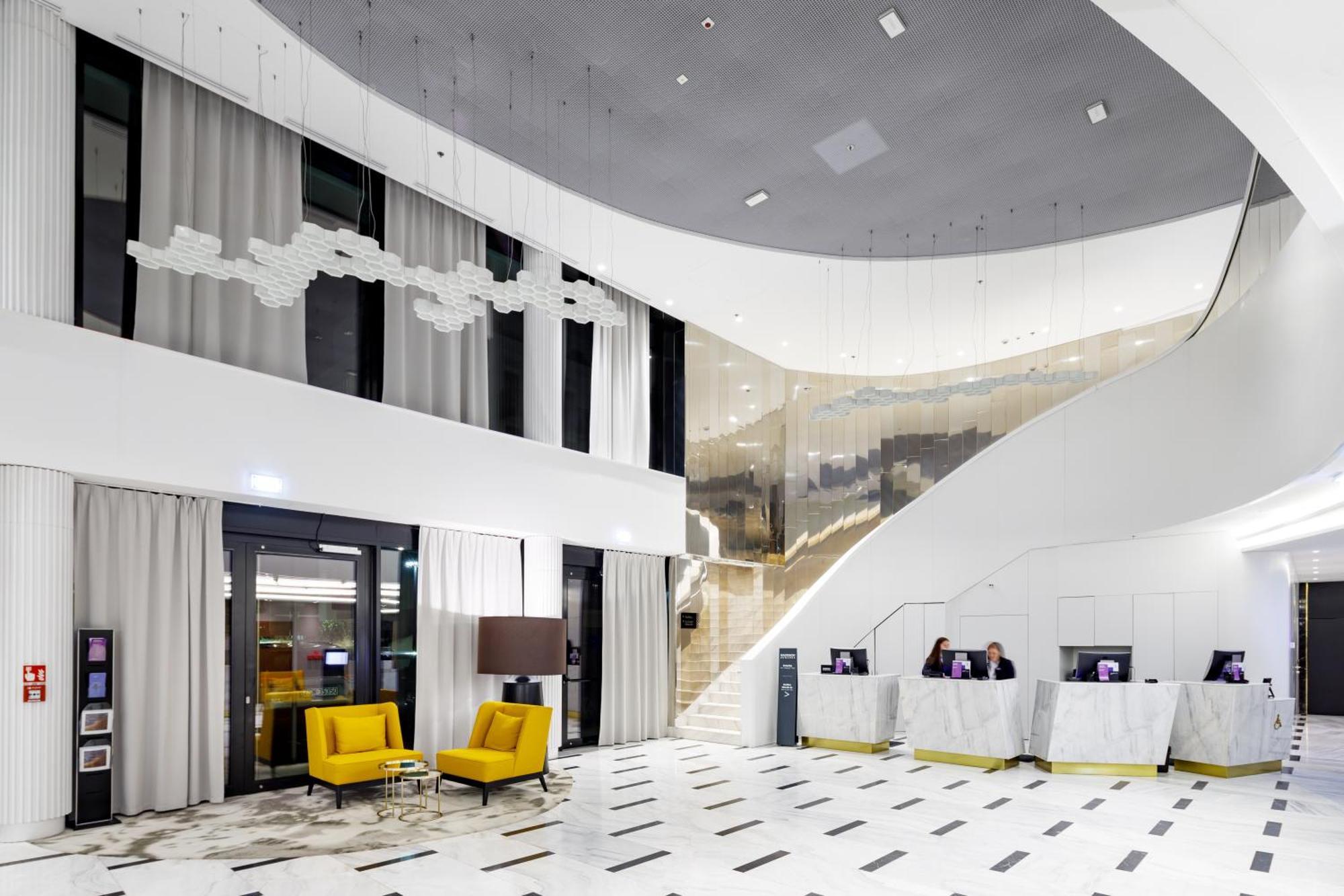 منتجع راديسون بلو سوينوجسي سفينويتشي المظهر الخارجي الصورة The photo shows a modern interior space, likely a hotel or a lobby area. It features a spacious, open design with high ceilings and a stylish staircase that leads to an upper level. The walls are mostly white, with large windows allowing natural ligh