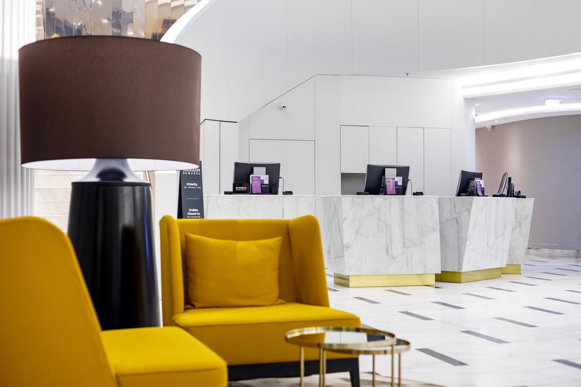 منتجع راديسون بلو سوينوجسي سفينويتشي المظهر الخارجي الصورة The photo shows a modern reception area, likely of a hotel or a similar establishment. In the foreground, there are two yellow armchairs with soft cushions, situated around a small round table with a minimalist design. Behind the seating area, there 