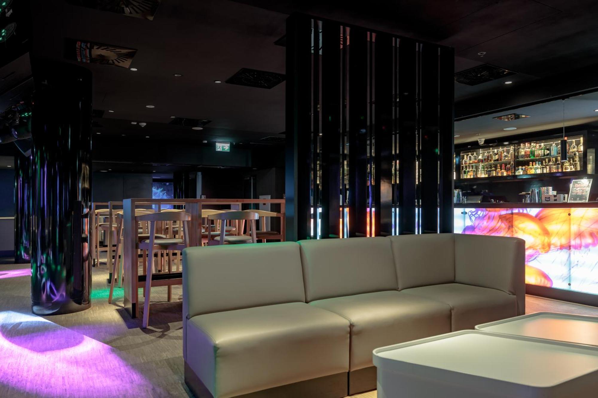 منتجع راديسون بلو سوينوجسي سفينويتشي المظهر الخارجي الصورة The photo shows the interior of a stylish lounge or bar. The space features a modern design with dark walls and a sleek atmosphere. There is a beige sectional sofa in the foreground, providing a casual seating area. In the background, a bar is visibl