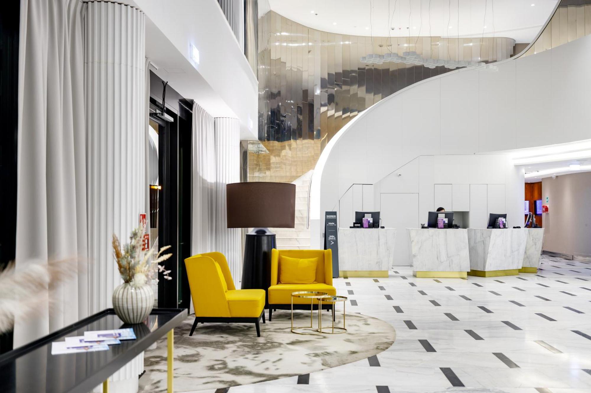 منتجع راديسون بلو سوينوجسي سفينويتشي المظهر الخارجي الصورة The photo shows the interior of a modern hotel lobby. The space features a stylish design with a combination of yellow and neutral-colored seating, including two yellow armchairs and a small table. In the background, there is a reception area with ma
