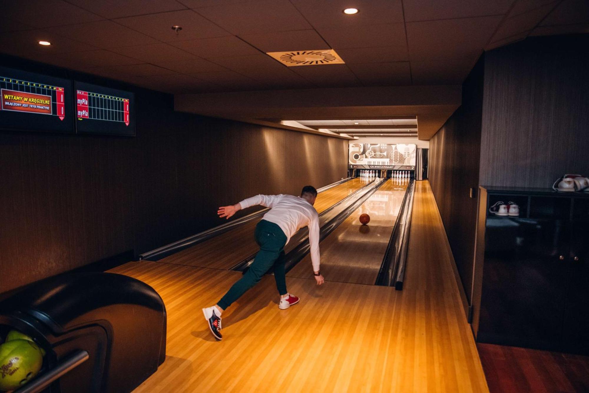 منتجع راديسون بلو سوينوجسي سفينويتشي المظهر الخارجي الصورة The photo shows a bowling alley. In the foreground, a person is throwing a bowling ball down the lane. They are wearing a white top and green pants, with red and white shoes. The bowling lane is made of polished wood, and at the end of the lane, ther