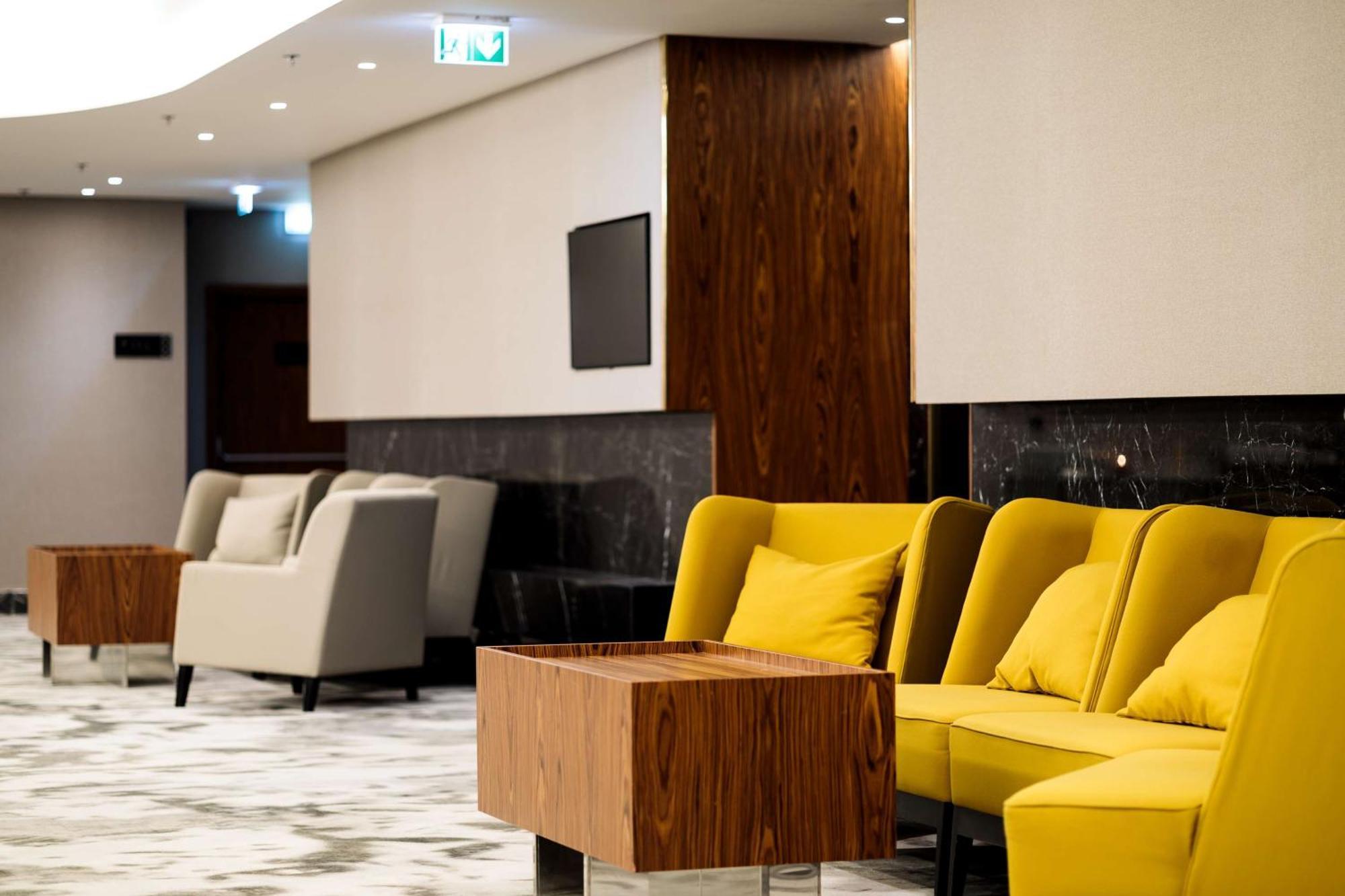 منتجع راديسون بلو سوينوجسي سفينويتشي المظهر الخارجي الصورة The photo depicts a modern lounge or waiting area with stylish seating. On the left, there are soft gray armchairs arranged around a wooden coffee table. In the center, there are yellow chairs with plush cushions, contributing a vibrant contrast to t