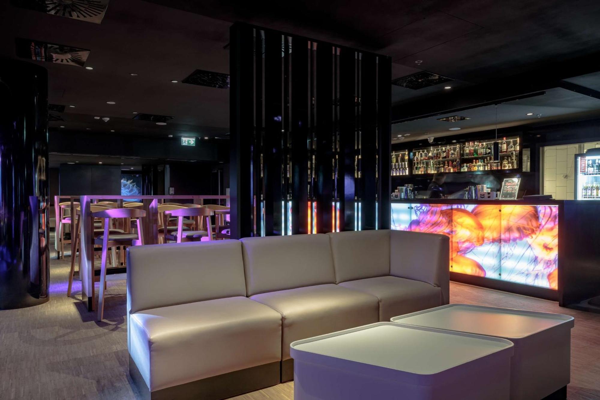 منتجع راديسون بلو سوينوجسي سفينويتشي المظهر الخارجي الصورة The photo depicts a modern interior space, possibly a lounge or bar. There are sleek, minimalistic furniture pieces, including a large, curved sofa and contemporary coffee tables. The lighting is dim, with a blend of colorful ambient lights illuminat