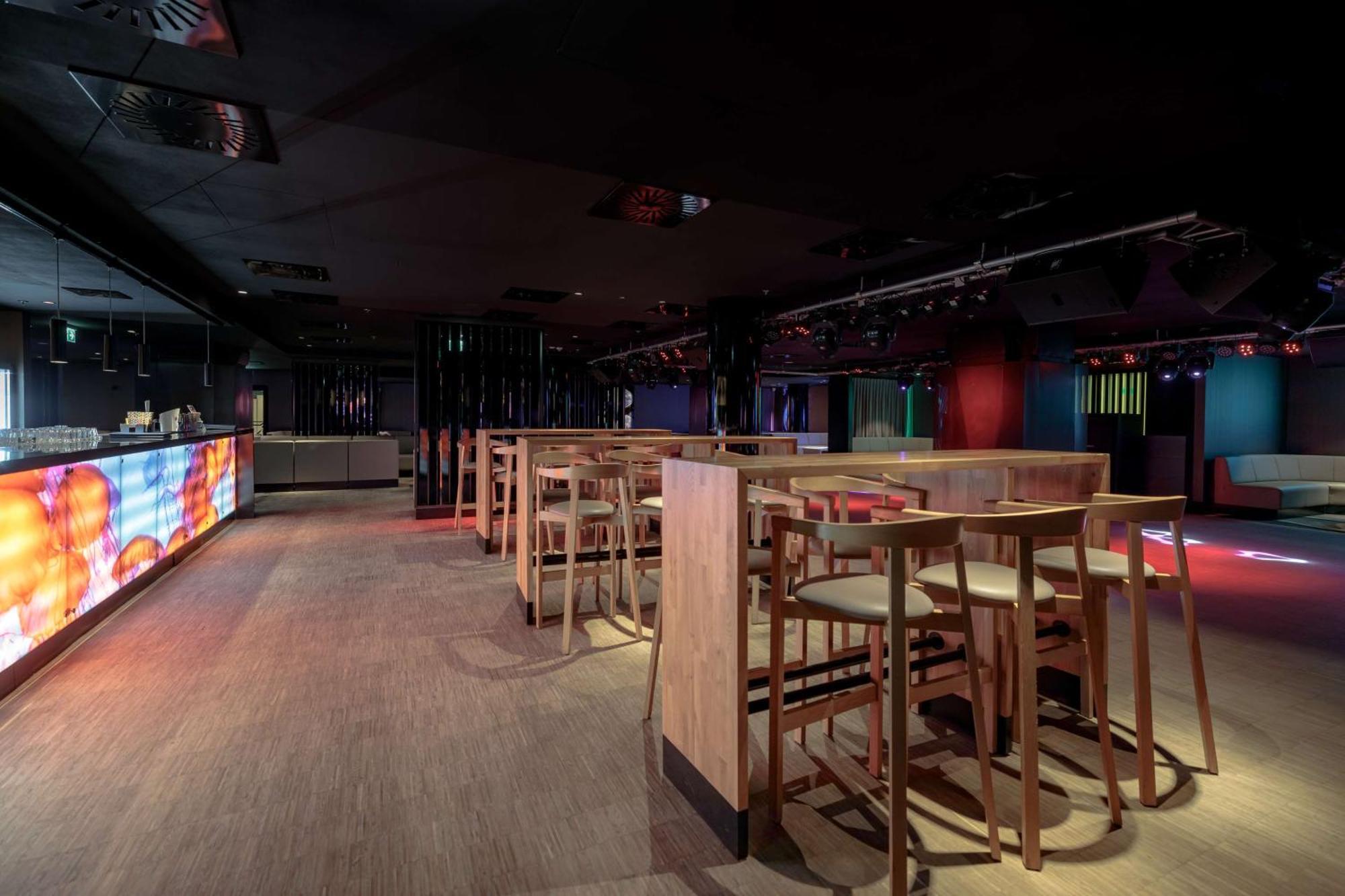 منتجع راديسون بلو سوينوجسي سفينويتشي المظهر الخارجي الصورة The photo shows an interior space that appears to be a bar or lounge. It features a modern design with a dark color scheme. There are several wooden high-top tables with matching stools arranged in the area. In the background, there is a bar counter,