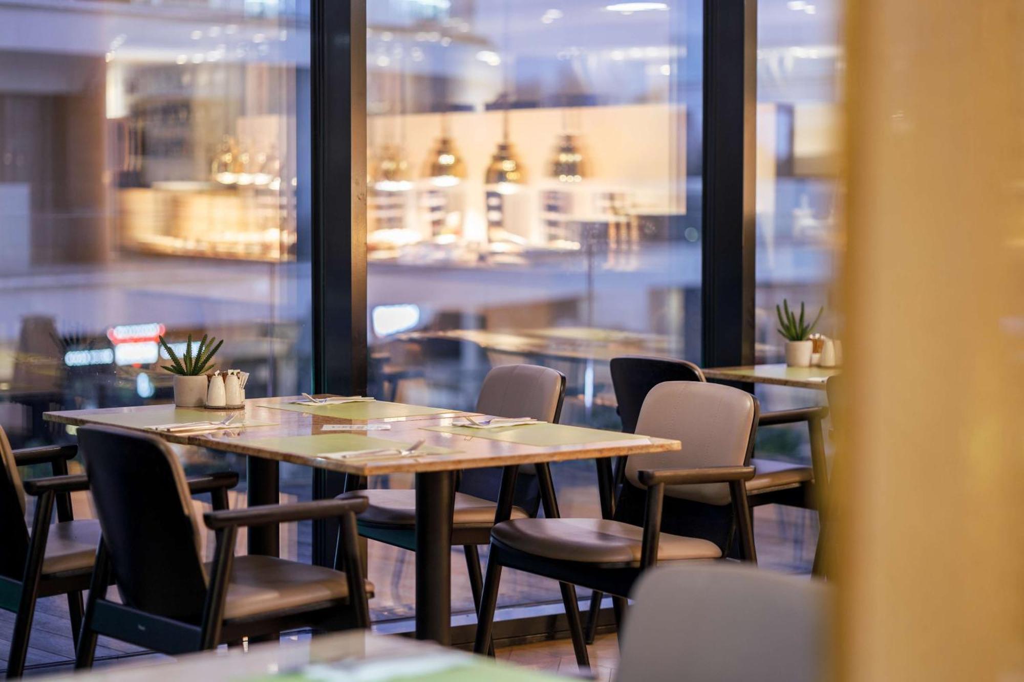 منتجع راديسون بلو سوينوجسي سفينويتشي المظهر الخارجي الصورة The photo shows a modern restaurant interior featuring several tables and chairs arranged under large windows. The tables are set with green placemats and cutlery. There are small potted plants on the tables, adding a touch of decor. In the backgroun