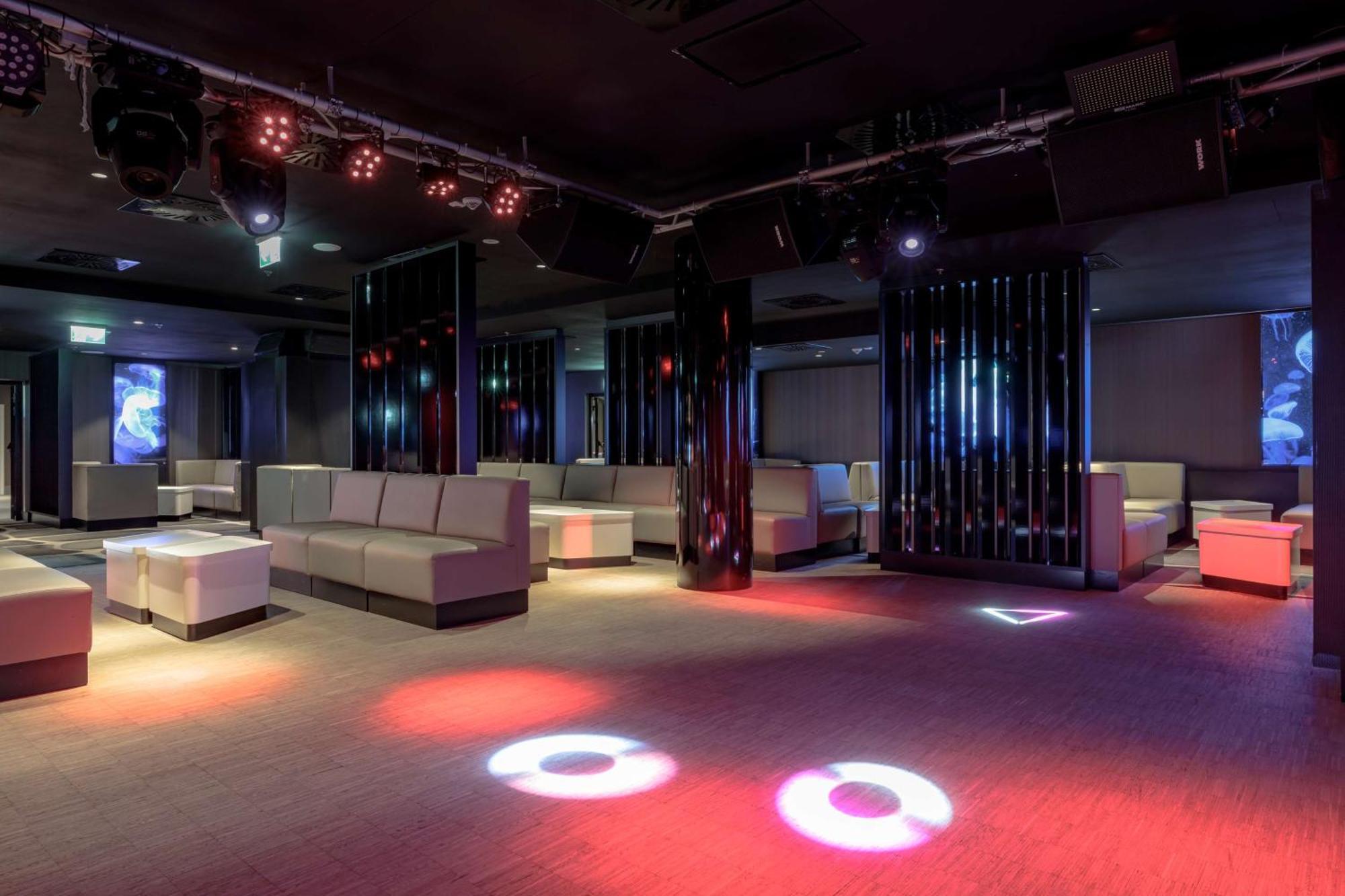 منتجع راديسون بلو سوينوجسي سفينويتشي المظهر الخارجي الصورة The photo depicts a modern nightclub interior, featuring a spacious layout with sleek, minimalist seating arrangements. The room has plush seating along the walls, and the floor is illuminated with circular lights in varying colors, creating a vibran