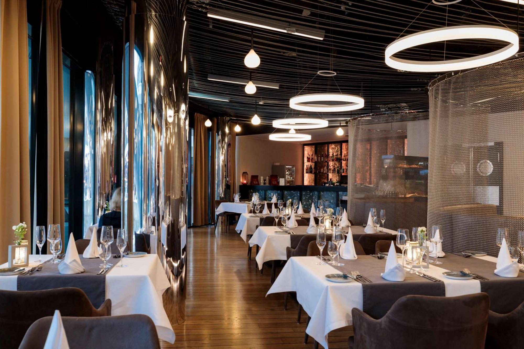 منتجع راديسون بلو سوينوجسي سفينويتشي المظهر الخارجي الصورة The photo shows the interior of a modern restaurant. It features elegantly set tables with white tablecloths and neatly arranged glassware. The design includes a sleek, contemporary aesthetic with dark walls and interesting lighting, including circul