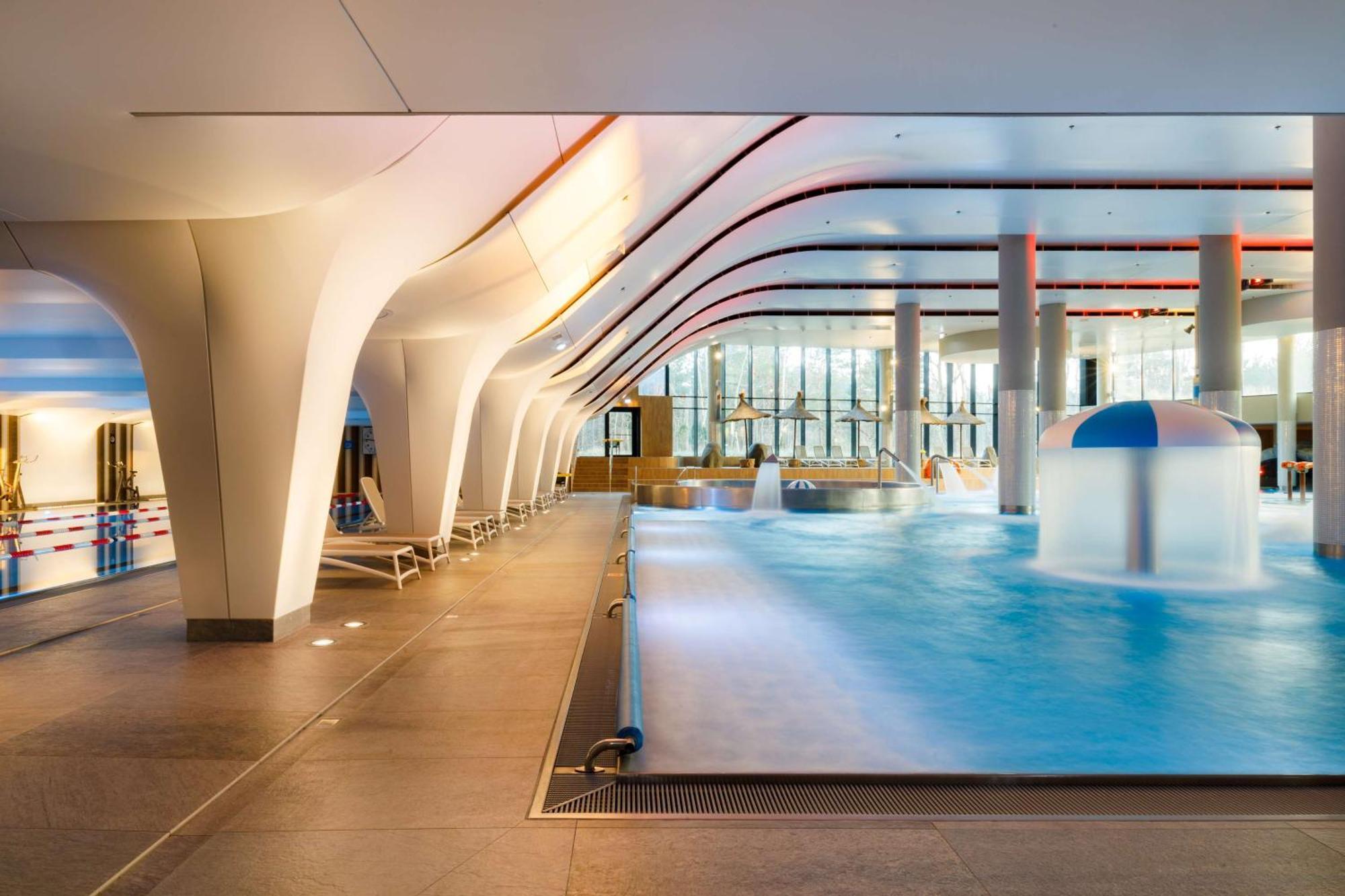 منتجع راديسون بلو سوينوجسي سفينويتشي المظهر الخارجي الصورة The photo shows an indoor swimming pool area with a modern architectural design. The space features large windows allowing natural light to enter, and the interior has smooth, flowing lines in the ceiling and columns. The pool has a light blue water 