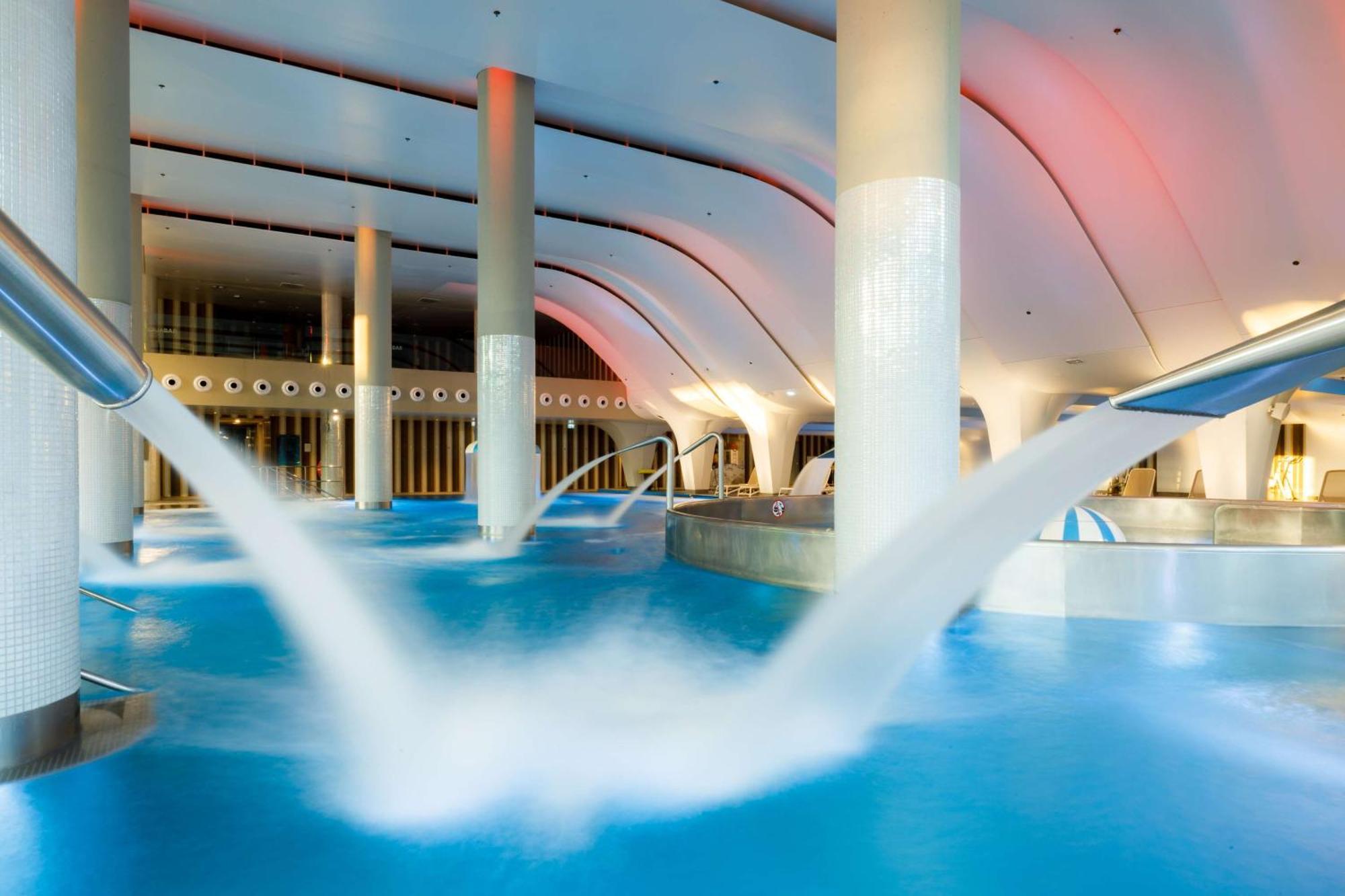 منتجع راديسون بلو سوينوجسي سفينويتشي المظهر الخارجي الصورة The photo depicts an indoor swimming pool area characterized by modern architecture. The pool is filled with clear blue water, and there are several columns supporting the ceiling. Water features, such as jets or fountains, are seen creating flowing 