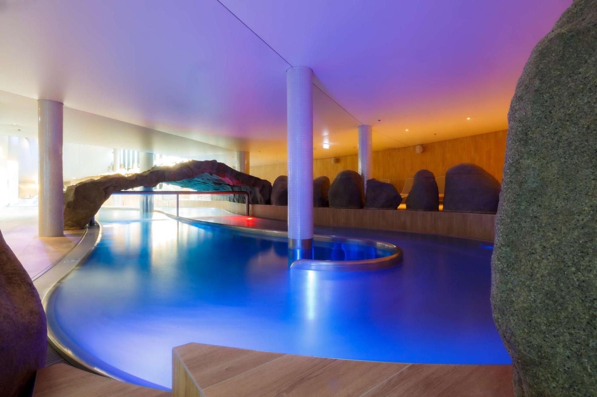 منتجع راديسون بلو سوينوجسي سفينويتشي المظهر الخارجي الصورة The photo showcases an elegant indoor swimming pool area. The pool has a flowing, organic shape and is illuminated with soft blue and purple lighting, creating a calming ambiance. Surrounding the pool are smooth, natural-looking stones and wooden ele