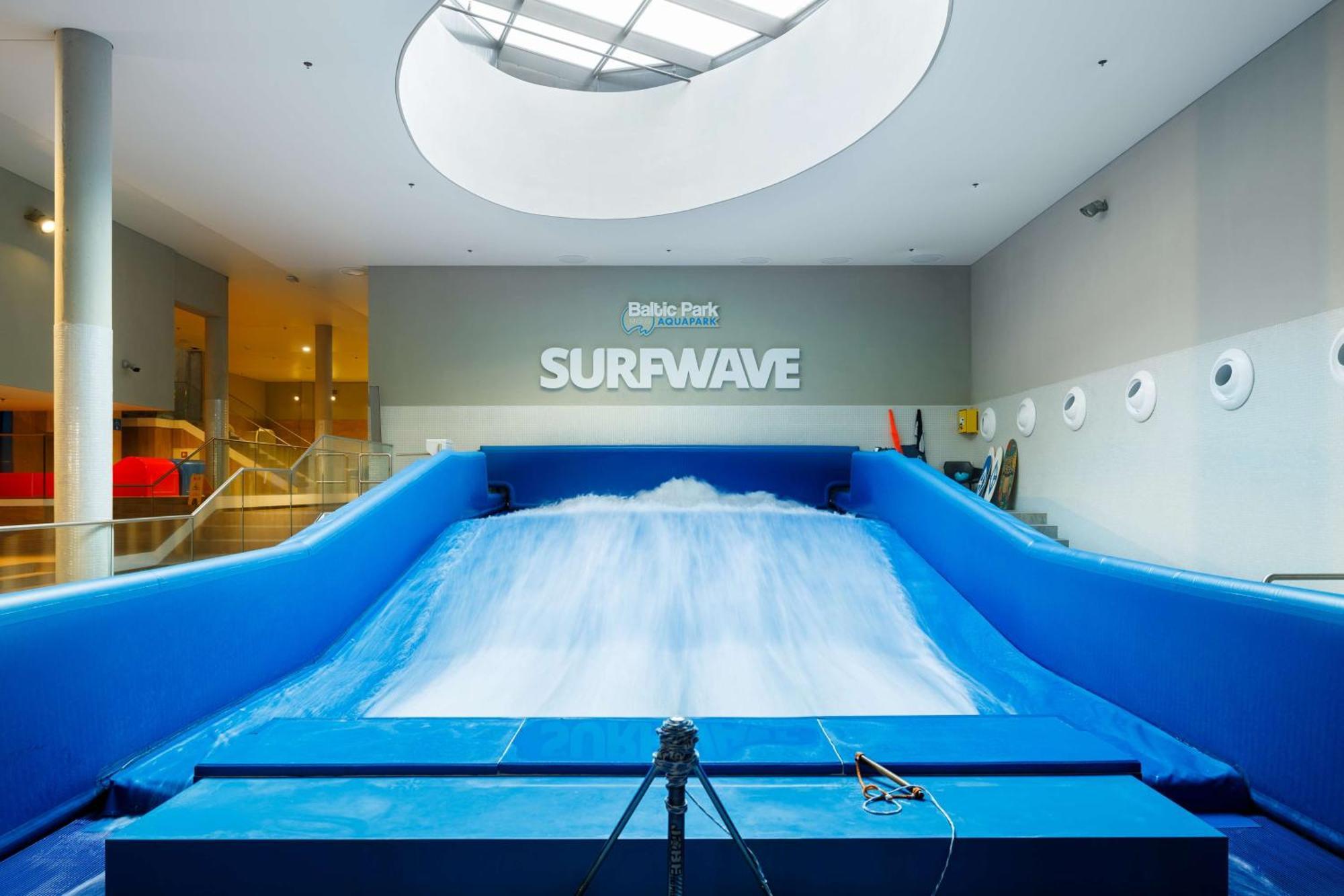 منتجع راديسون بلو سوينوجسي سفينويتشي المظهر الخارجي الصورة The photo shows an indoor surfing attraction called "Surfwave." It features a large blue ramp with water flowing down it, creating a wave-like effect for surfing. Above the ramp, there is a sign that says "SURFWAVE." The area appears well-lit and mod